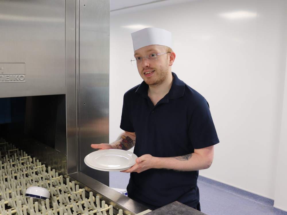 Young man with glasses holding a plate in a commercial kitchen