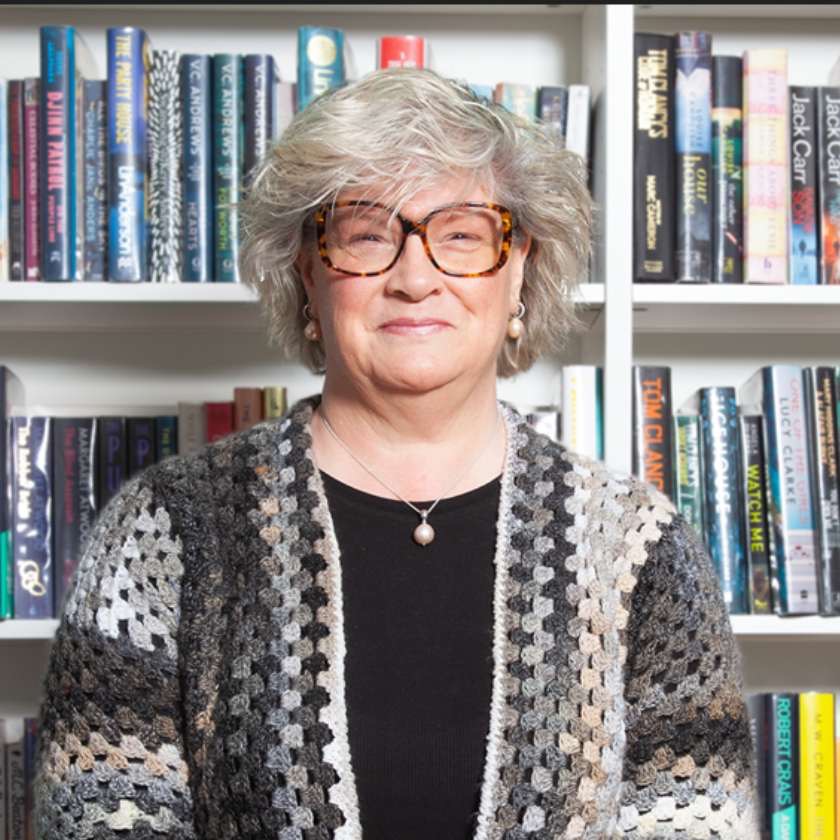 Mature woman with glasses smiling in front of a bookcase
