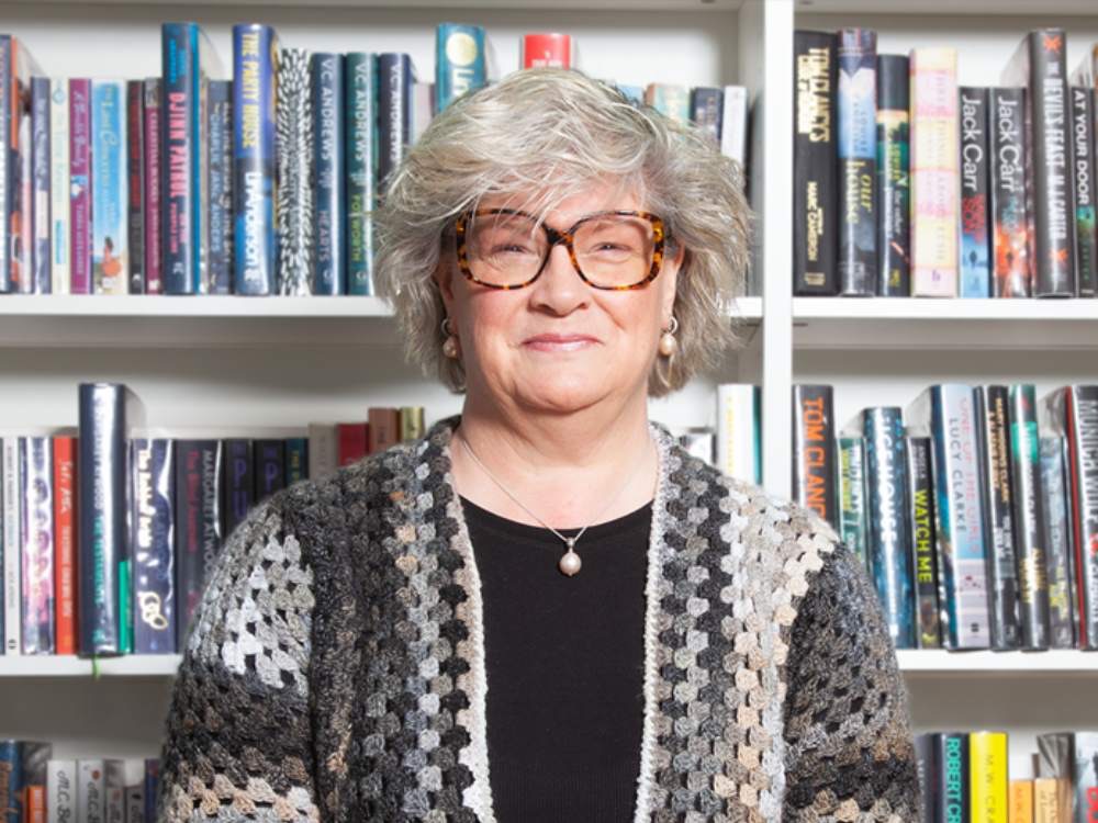 Mature woman with glasses smiling in front of bookcase