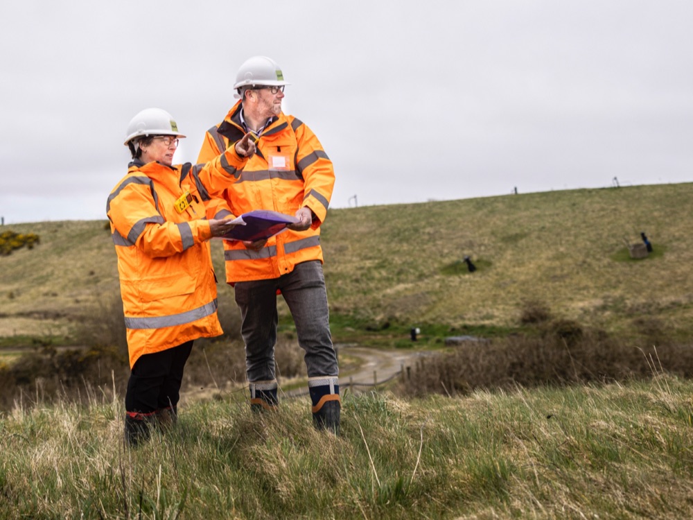 Man and woman in high visibility jackets on hillside