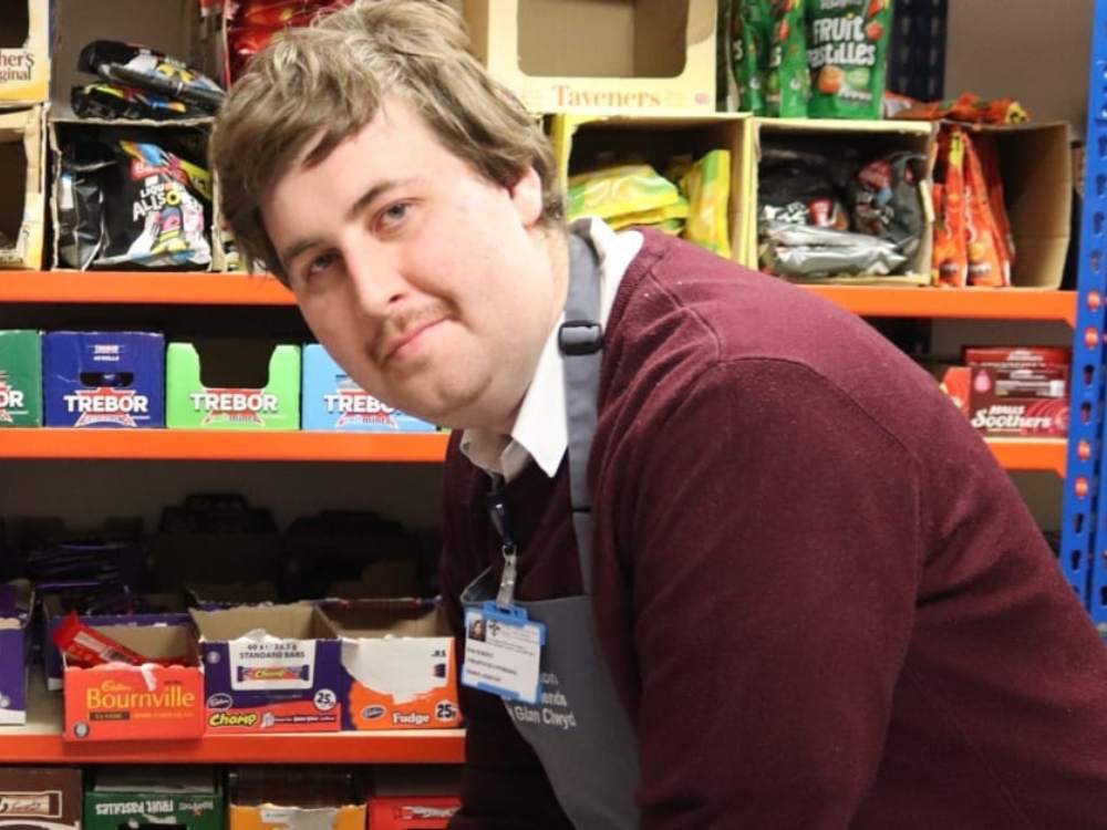 Young adult in workwear standing in front of shelves in shop