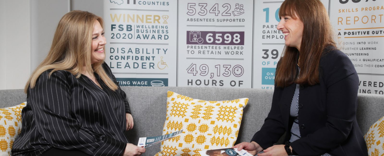 Two women sitting on sofa at work talking and smiling