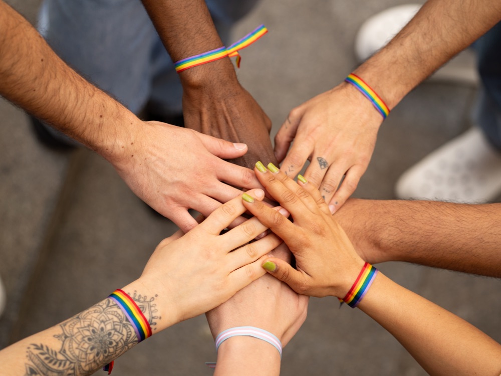 Seven hands of different skin colour overlaid and touching