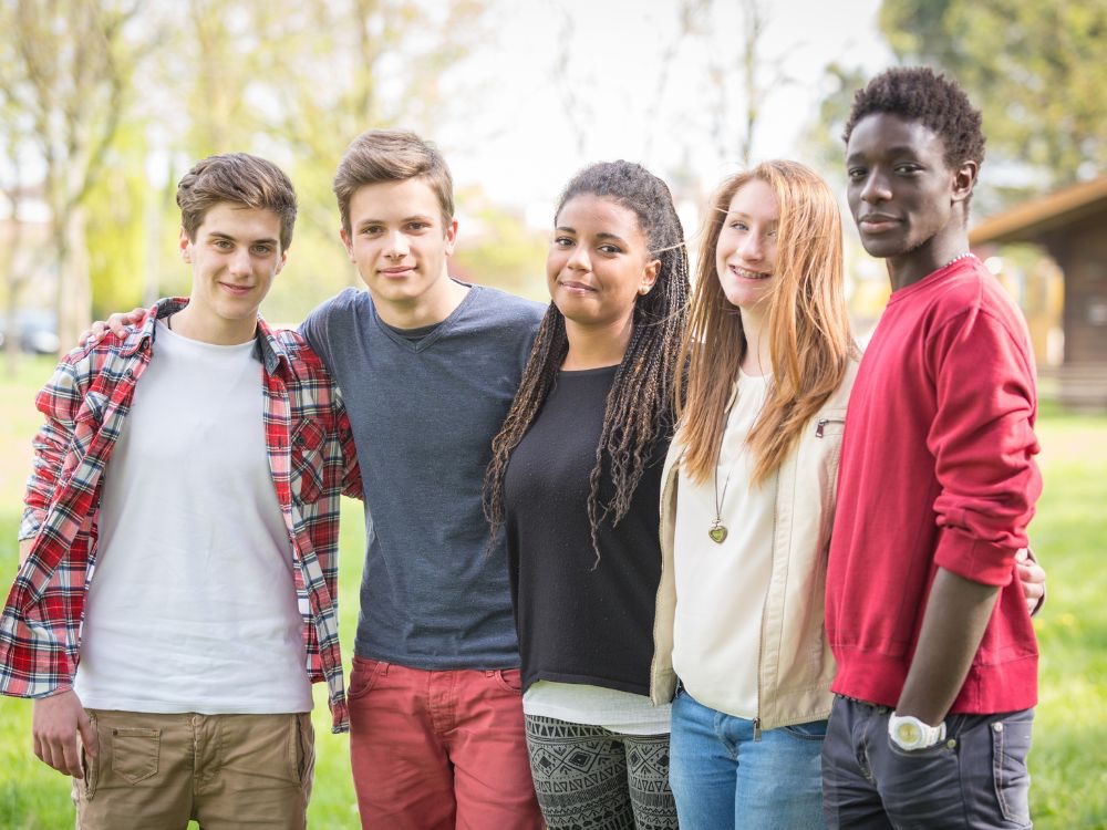 Five teenagers standing together outside smiling