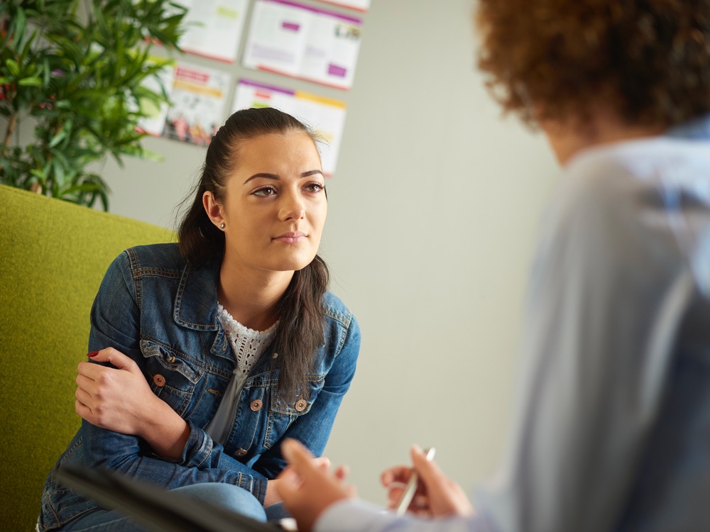 Young woman in denim jacket on sofa listening to therapist