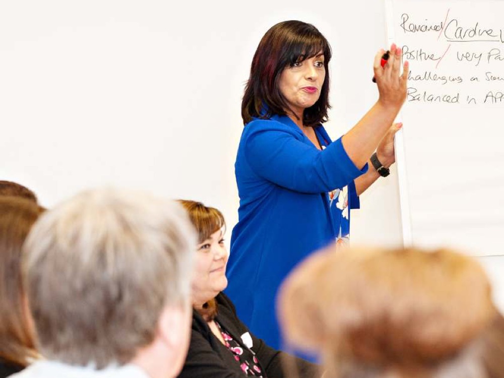 Woman in blue cardigan presenting in front of a seated audience