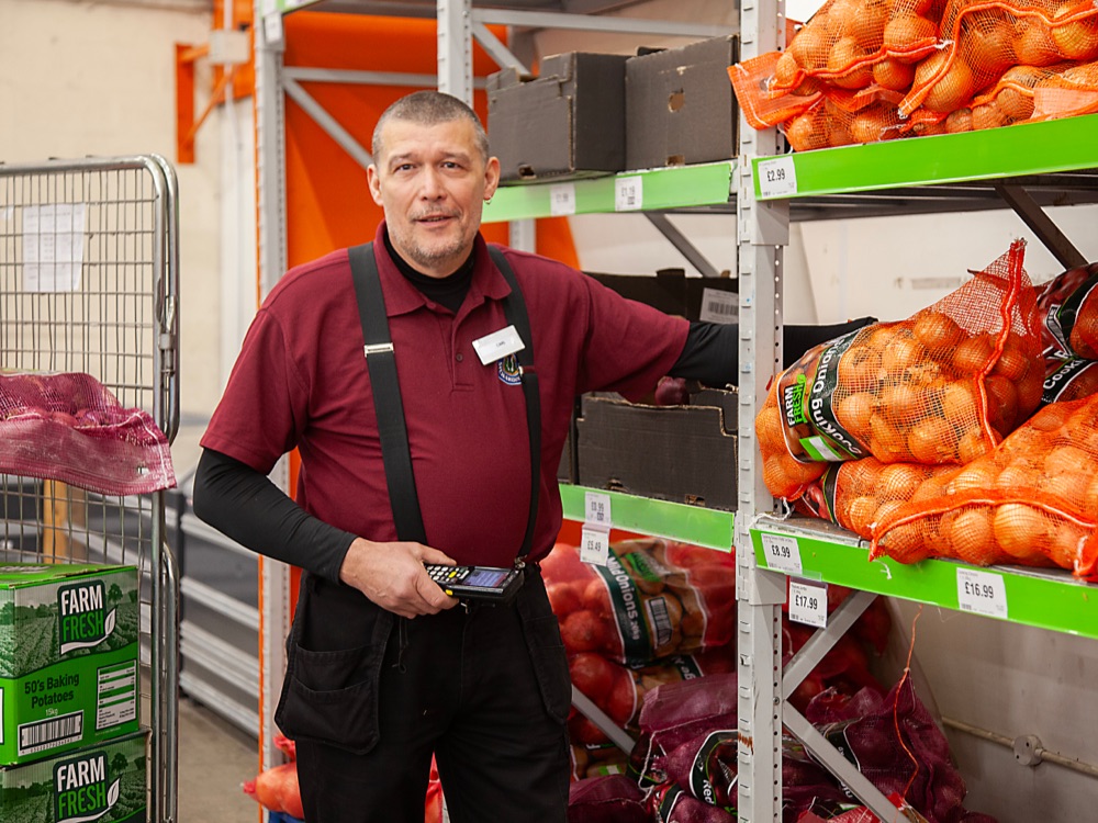 Mature male factory worker standing by shelves full of vegetables