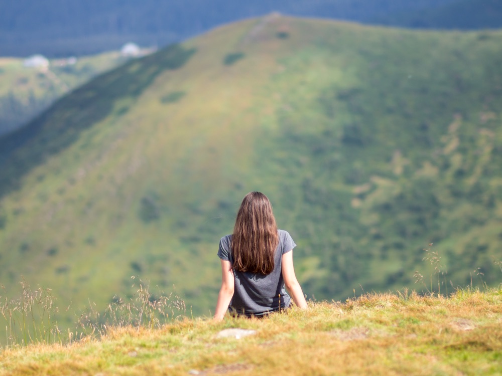 Young woman sitting alone on grass looking over green hills