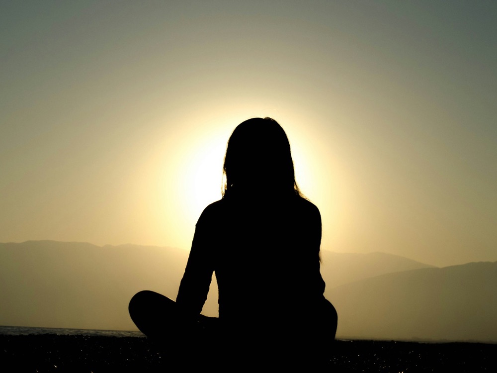 Silhouette of a woman sitting alone on a hillside at sunset