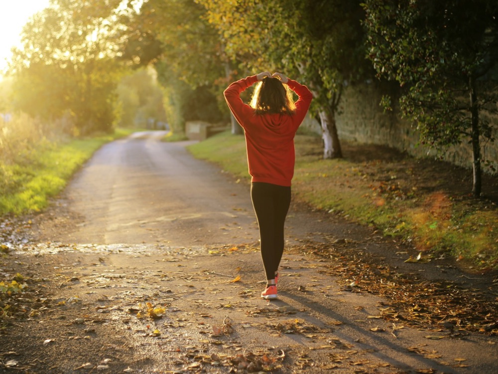 Young adult jogger standing alone on a country road at sunset with hands on head