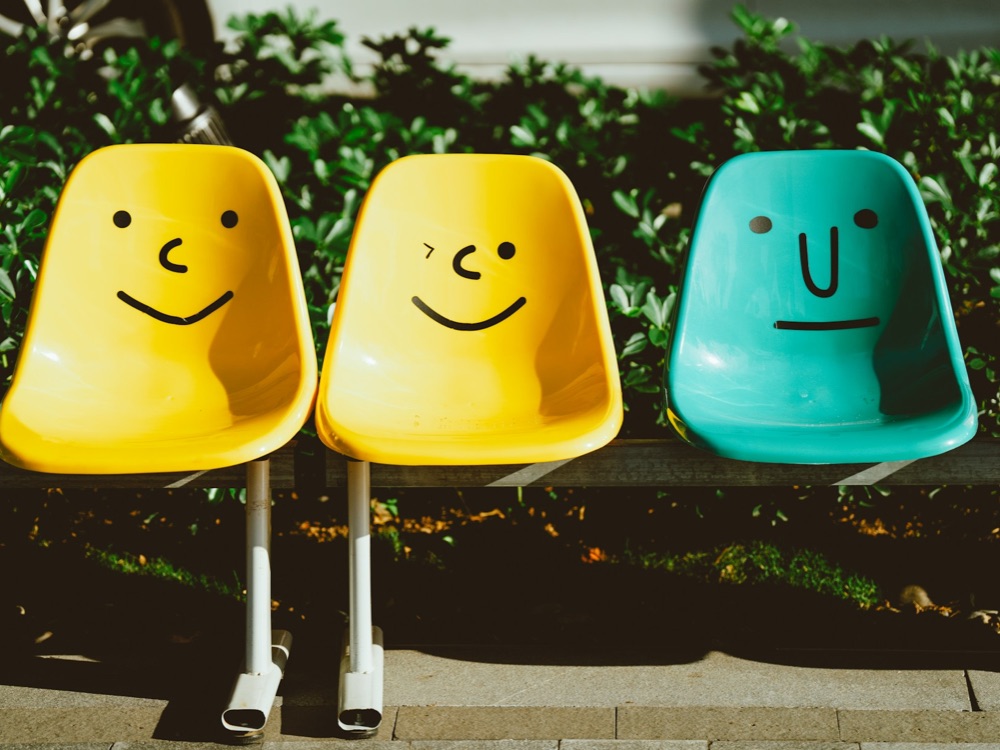 Three outdoor plastic seats with faces drawn on them with mixed expressions