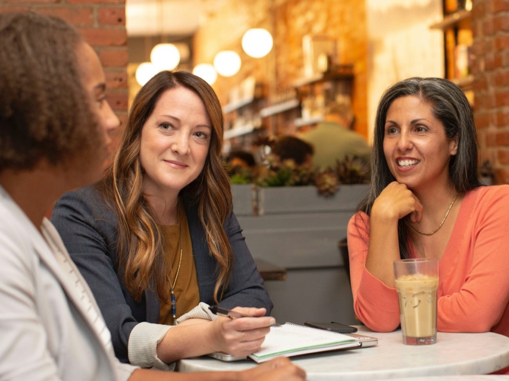 Two women interviewing another woman in a coffee shop