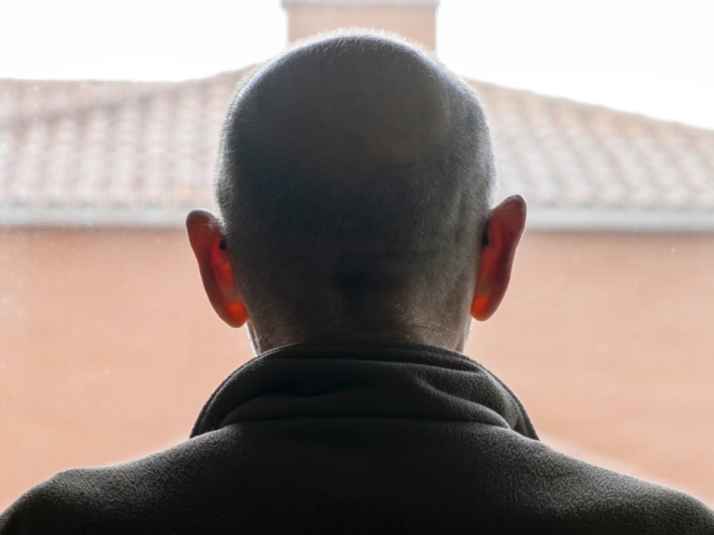 Silhouette of elderly man looking out of window at home
